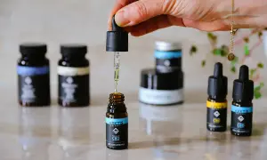 En hand droppar olja från en pipett ner i en liten flaska. Flera flaskor med CBD-olja, inklusive en med MCT-olja, står uppradade.
