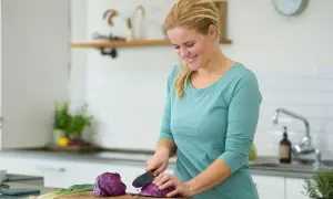 Kvinna hackar rödkål i köket, en del av en antiinflammatorisk kost som kan inkludera potatis.
