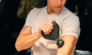 En man använder en Rubicson massagepistol mini för att massera sin arm.