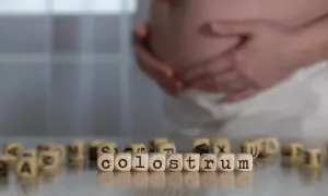 Gravid mage med händerna vilande på magen. Träpärlor med bokstäver bildar ordet "colostrum svenska", som beskriver den första mjölken.