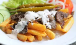 En tallrik med pommes frites, kebabkött, vit sås, sallad, gurka, tomat, lök och inlagda paprikor. Ett perfekt kebab recept för en snabb middag.