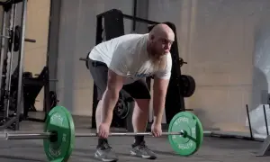 Man med skägg förbereder sig för stela marklyft med en skivstång laddad med gröna vikter.