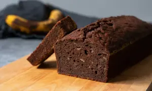 En saftig banankaka i långpanna, med en skiva uppskuren. En övermogen banan ligger i bakgrunden.