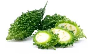 Gröna, taggiga bitter melonfrukter, en hel och några skivade, visar sitt ljusa inre.