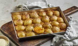 Ugnsbakade potatishalvor, gyllene och kryddade, redo att serveras. En sked visar den mjuka insidan av en perfekt rostad potatis.