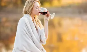 Kvinna med blont hår dricker rödvin insvept i en filt. Visste du att kalorier vitt vin per dl kan variera?