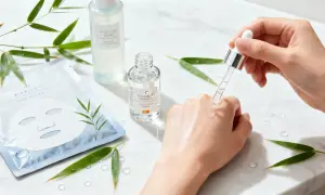En hand applicerar C-vitaminserum för j beauty. Bambublad och sheet mask i bakgrunden.