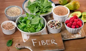 En skärbräda med texten "FIBER" omgiven av skålar med bönor, linser, spenat, sockerärtor, hallon, avokado, päron och korn. En hyllning till fiberrik mat.