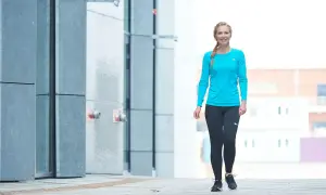 En kvinna i träningskläder ler och promenerar varje dag 1 timme längs en modern byggnad.