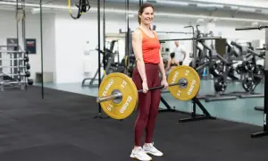 Tjej redo för marklyft startvikt med en skivstång med 15 kg vikter på varje sida.