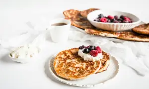 En härlig keto diet frukost med pannkakor, grädde och bär. En kopp kaffe står bredvid.