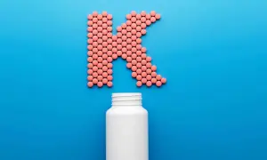 Rosa piller formar bokstaven K, med en tom vit burk nedanför. Kan det finnas k2-vitamin biverkningar?