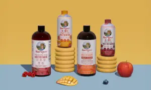 Flera flaskor Mary Ruths multivitamin i olika smaker, inklusive barnvarianten. Frukt som hallon, mango och äpple finns bredvid.