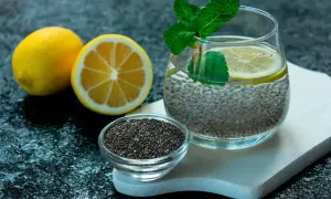 Ett glas med chia vatten, garnerat med citron och mynta. Bredvid står en skål med chiafrön och två citroner.