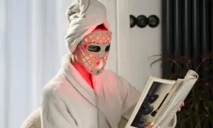 Person med handduk på huvudet och en led mask ansikte läser en bok i en morgonrock.