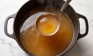 En slev lyfter gyllene, ångande buljong från en gjutjärnsgryta. Doften av real broth savory spices sprider sig.