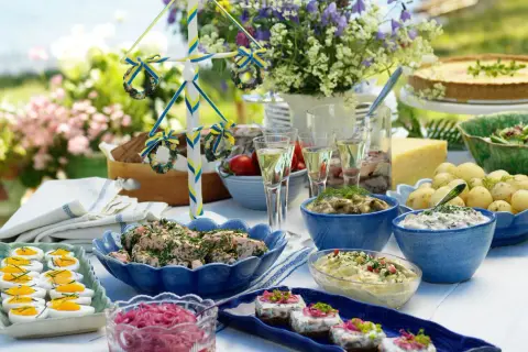 En härlig midsommar buffe med sill, potatis, ägg och en paj. En midsommarstång i bakgrunden.