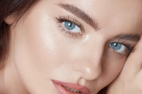 Närbild på en kvinna med blå ögon och perfekt makeup. Hennes ögonbryn ger en illusion av ett "brow lift".