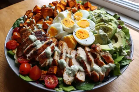 En stor, matig sallad med grillad kyckling, ägg, sötpotatis, avokado och tomater, toppad med en krämig dressing.