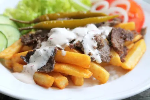 En tallrik med pommes frites, kebabkött, vit sås, sallad, gurka, tomat, lök och inlagda paprikor. Ett perfekt kebab recept för en snabb middag.