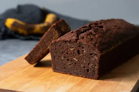 En saftig banankaka i långpanna, med en skiva uppskuren. En övermogen banan ligger i bakgrunden.