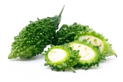 Gröna, taggiga bitter melonfrukter, en hel och några skivade, visar sitt ljusa inre.