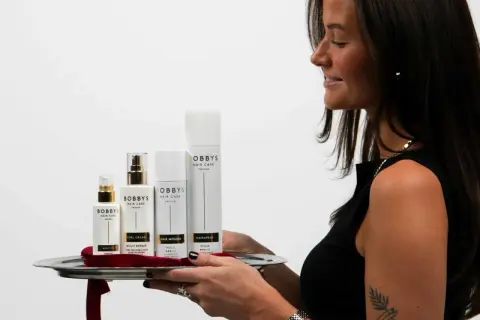 En kvinna presenterar en bricka med Bobby's Hair Care-produkter, inklusive Bobby's Curl Cream, för perfekt lockigt hår.