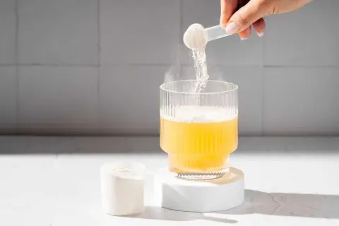 En hand häller pulver från en skopa ner i ett glas med gul vätska. Pulvret är en del av matters multi collagen.