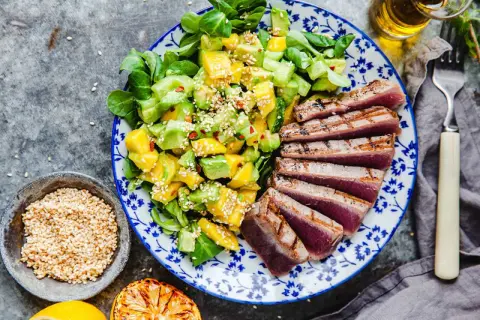 En tallrik med grillad tonfisk och en fräsch sallad på mango och avokado, toppad med sesamfrön.