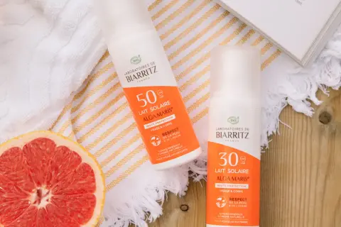 Två solkrämer från Biarritz med naturliga ingredienser, en med SPF 50 och en med SPF 30, ligger bredvid en grapefrukt och en bok.