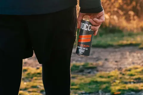 Person in athletic wear holding a NOCCO FOCUS energy drink can outdoors.