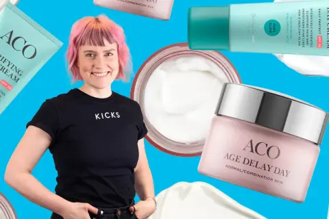 En kvinna med rosa hår ler omgiven av ACO-produkter, inklusive ACO ansiktskräm anti age.