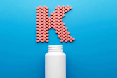 Rosa piller formar bokstaven K, med en tom vit burk nedanför. Kan det finnas k2-vitamin biverkningar?