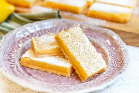 Citronkaka i långpanna, pudrad med florsocker, serveras på en vacker lila tallrik. Perfekt för fikat!