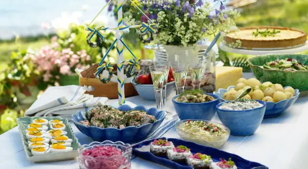 En härlig midsommar buffe med sill, potatis, ägg och en paj. En midsommarstång i bakgrunden.