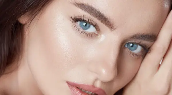 Närbild på en kvinna med blå ögon och perfekt makeup. Hennes ögonbryn ger en illusion av ett "brow lift".