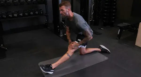 Man stretchar på en matta i gymmet, förbereder sig för träning med lårcurl maskin.