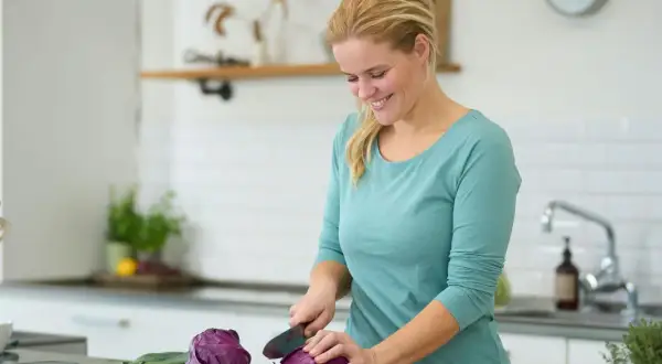 Kvinna hackar rödkål i köket, en del av en antiinflammatorisk kost som kan inkludera potatis.