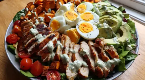 En stor, matig sallad med grillad kyckling, ägg, sötpotatis, avokado och tomater, toppad med en krämig dressing.