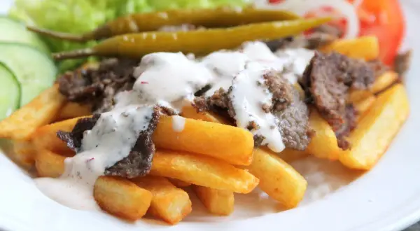 En tallrik med pommes frites, kebabkött, vit sås, sallad, gurka, tomat, lök och inlagda paprikor. Ett perfekt kebab recept för en snabb middag.