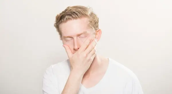 Man med slutna ögon och hand över munnen, kan vara ett tecken på l-lysin brist symtom som trötthet eller svaghet.