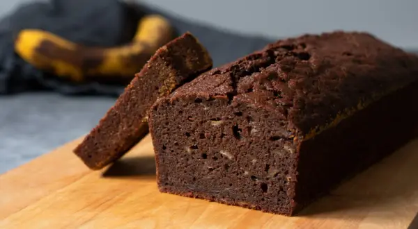En saftig banankaka i långpanna, med en skiva uppskuren. En övermogen banan ligger i bakgrunden.