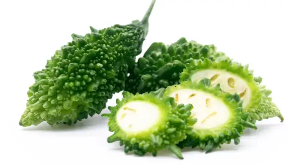Gröna, taggiga bitter melonfrukter, en hel och några skivade, visar sitt ljusa inre.