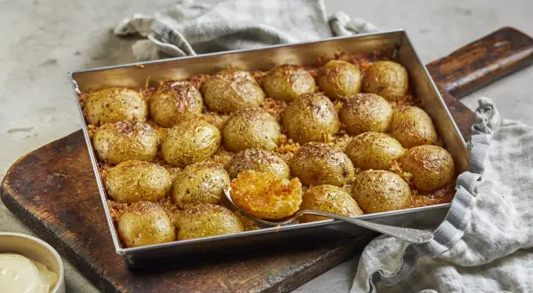 Ugnsbakade potatishalvor, gyllene och kryddade, redo att serveras. En sked visar den mjuka insidan av en perfekt rostad potatis.