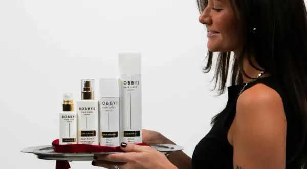 En kvinna presenterar en bricka med Bobby's Hair Care-produkter, inklusive Bobby's Curl Cream, för perfekt lockigt hår.