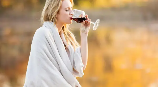 Kvinna med blont hår dricker rödvin insvept i en filt. Visste du att kalorier vitt vin per dl kan variera?