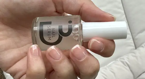 En hand håller en flaska nagelserum. Naglarna ser friska och starkare ut efter användning.