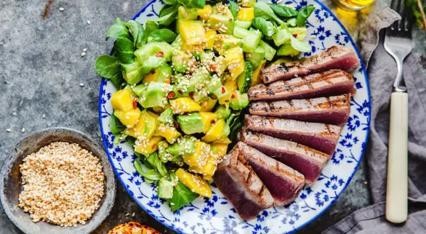 En tallrik med grillad tonfisk och en fräsch sallad på mango och avokado, toppad med sesamfrön.