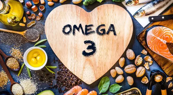 En hjärtformad träskiva med texten "OMEGA 3" omgiven av lax, sardiner, räkor, nötter, frön, broccoli och olivolja. En hälsosam måltid!
