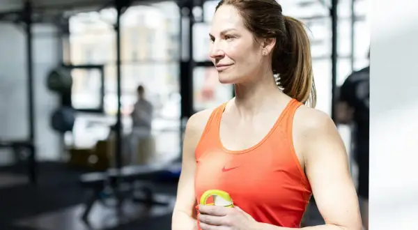Kvinna med axelpress muskler i gym, håller en vattenflaska.